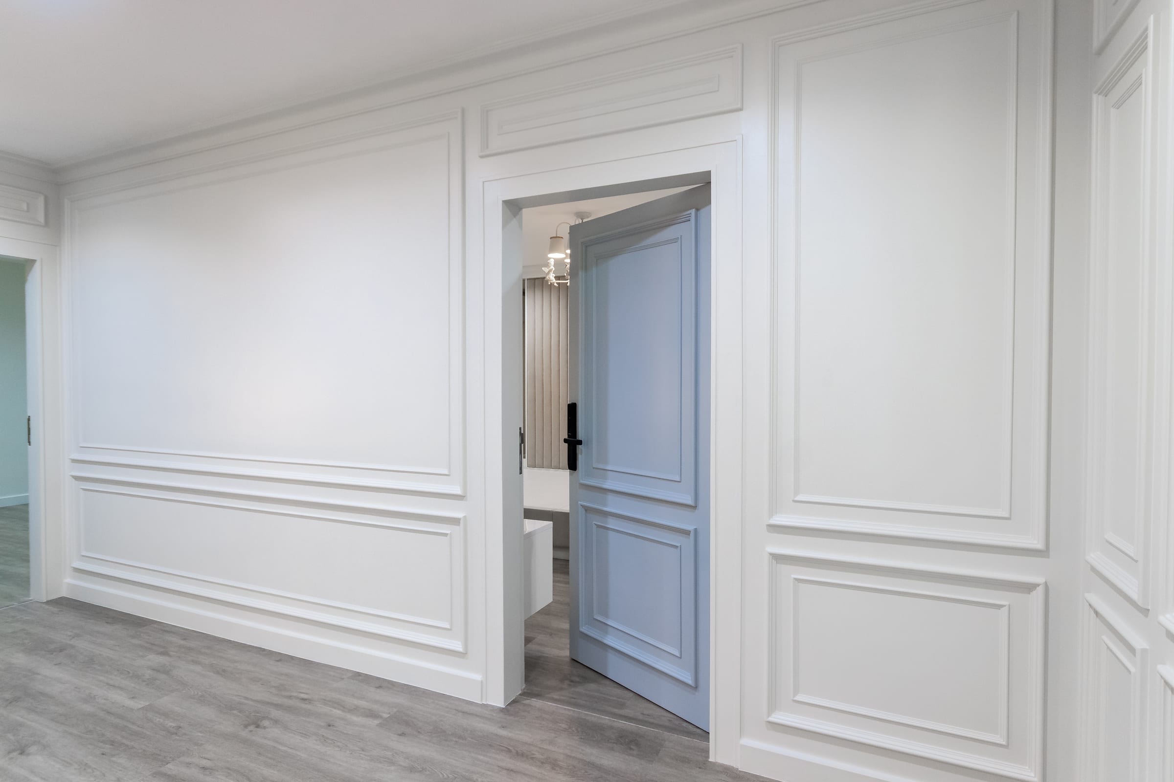 Corredor com boiserie branca em molduras retangulares e porta azul-pastel