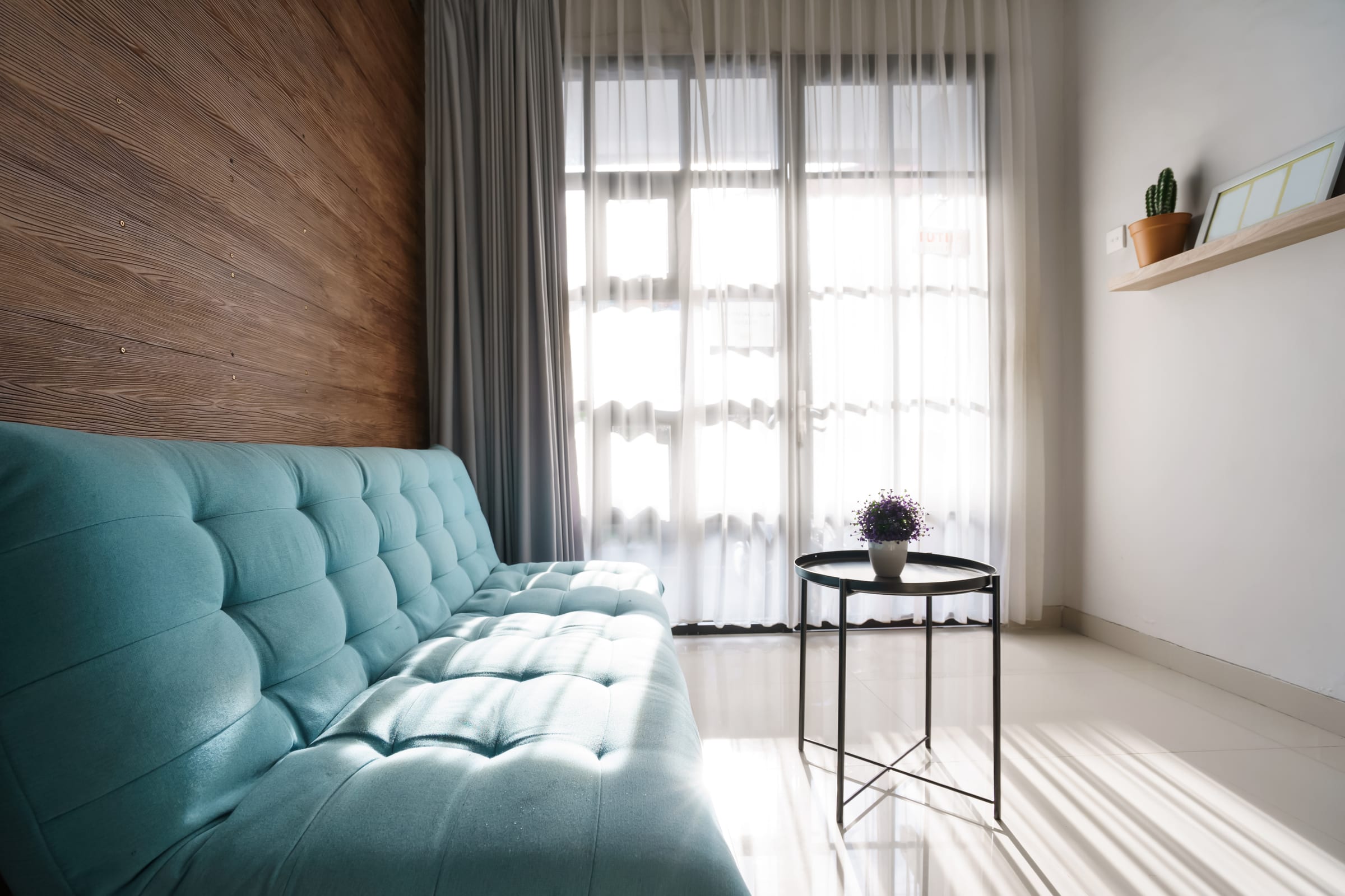 Sala com parede ripada em madeira clara, voil branco e sofá turquesa
