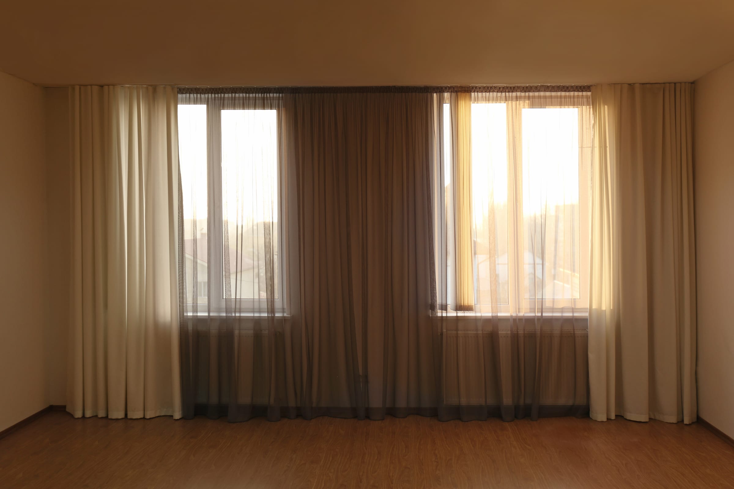 Sala vazia com cortinas duplas creme e voil cinza no fim da tarde
