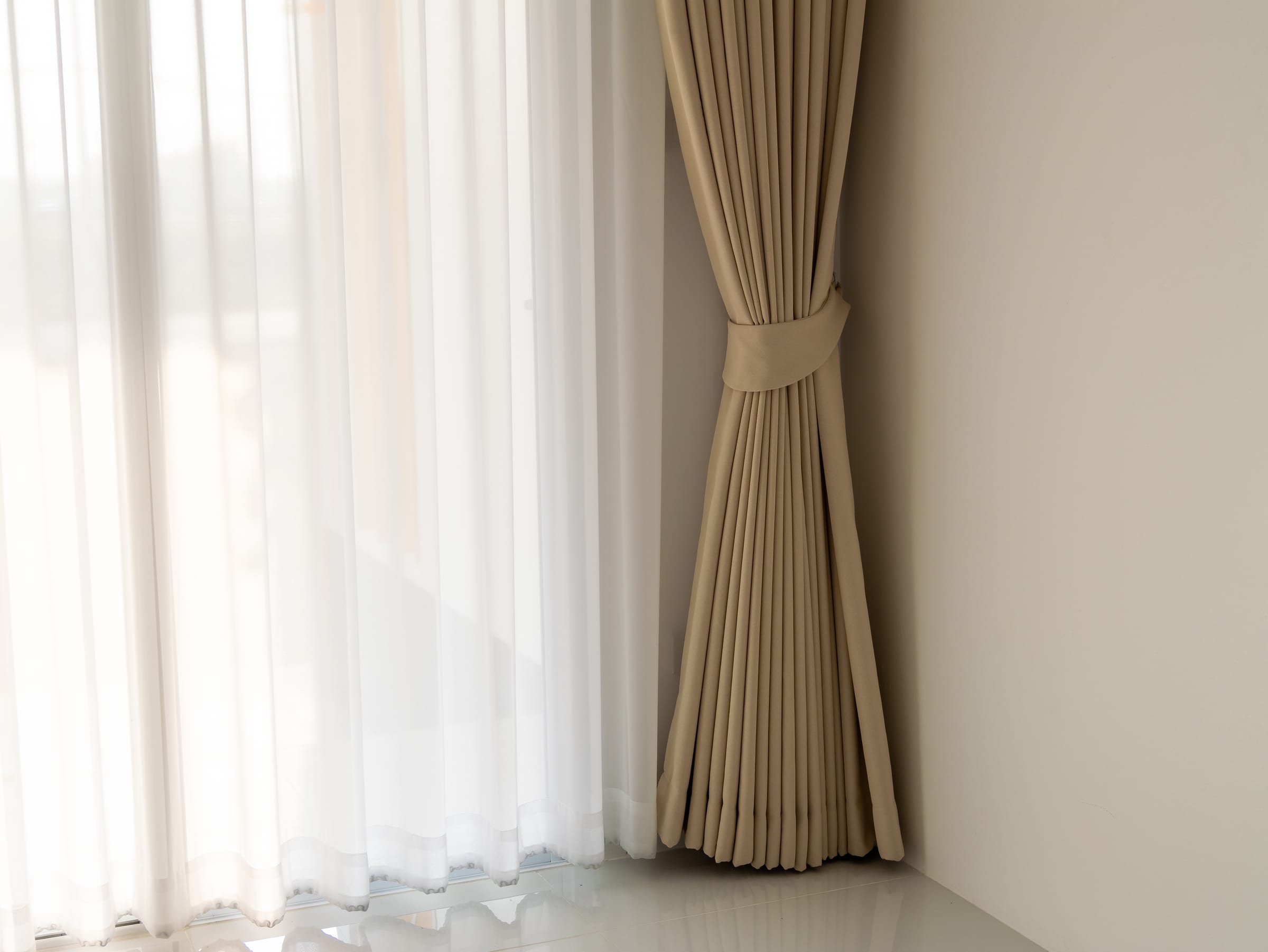 Detalhe de cortina blackout bege com voil branco e tie-back