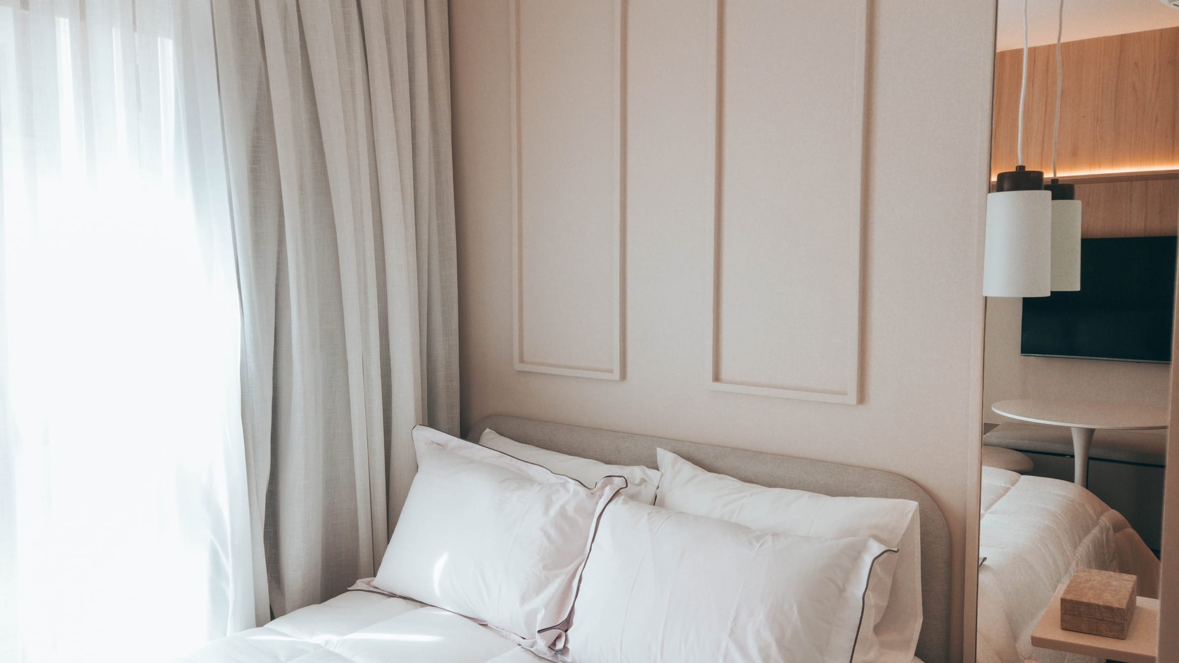 Quarto com boiserie bege, voil branco e cortina cinza ao fundo