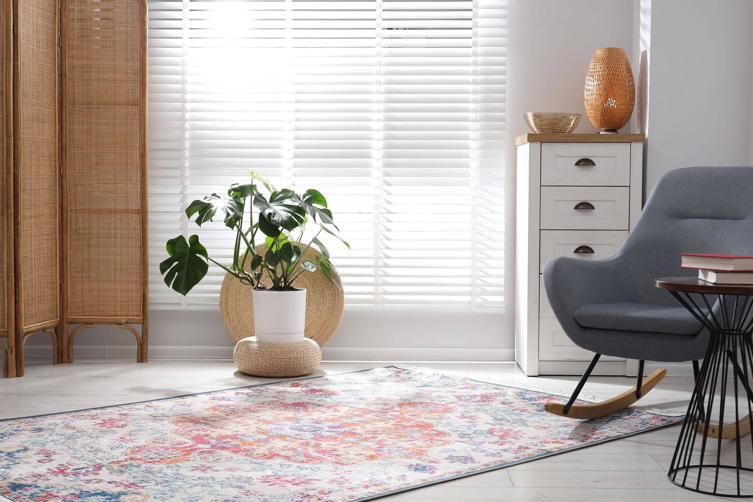 Sala clara com persianas horizontais brancas, monstera e biombo de palha