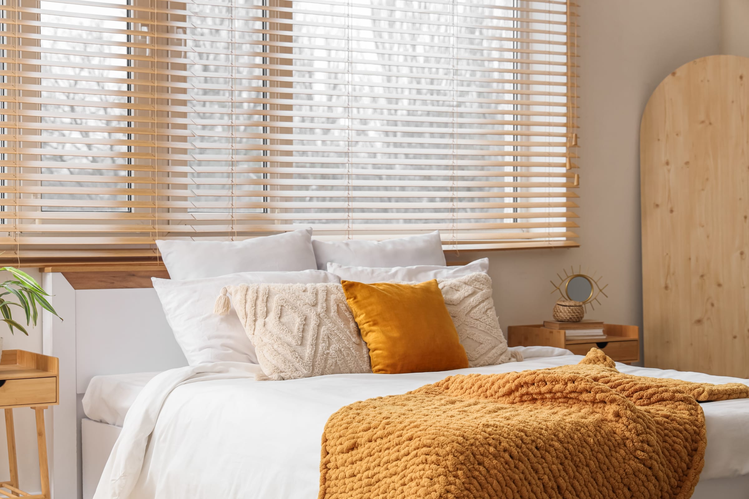 Quarto com persianas horizontais brancas e roupa de cama em tons mostarda